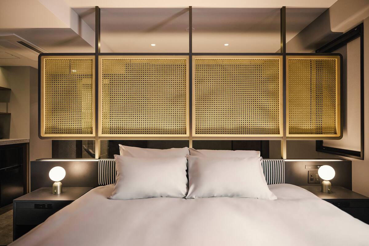 Een moderne hotelkamer met een groot bed, twee nachtkastjes met lampen en een decoratief wandpaneel.