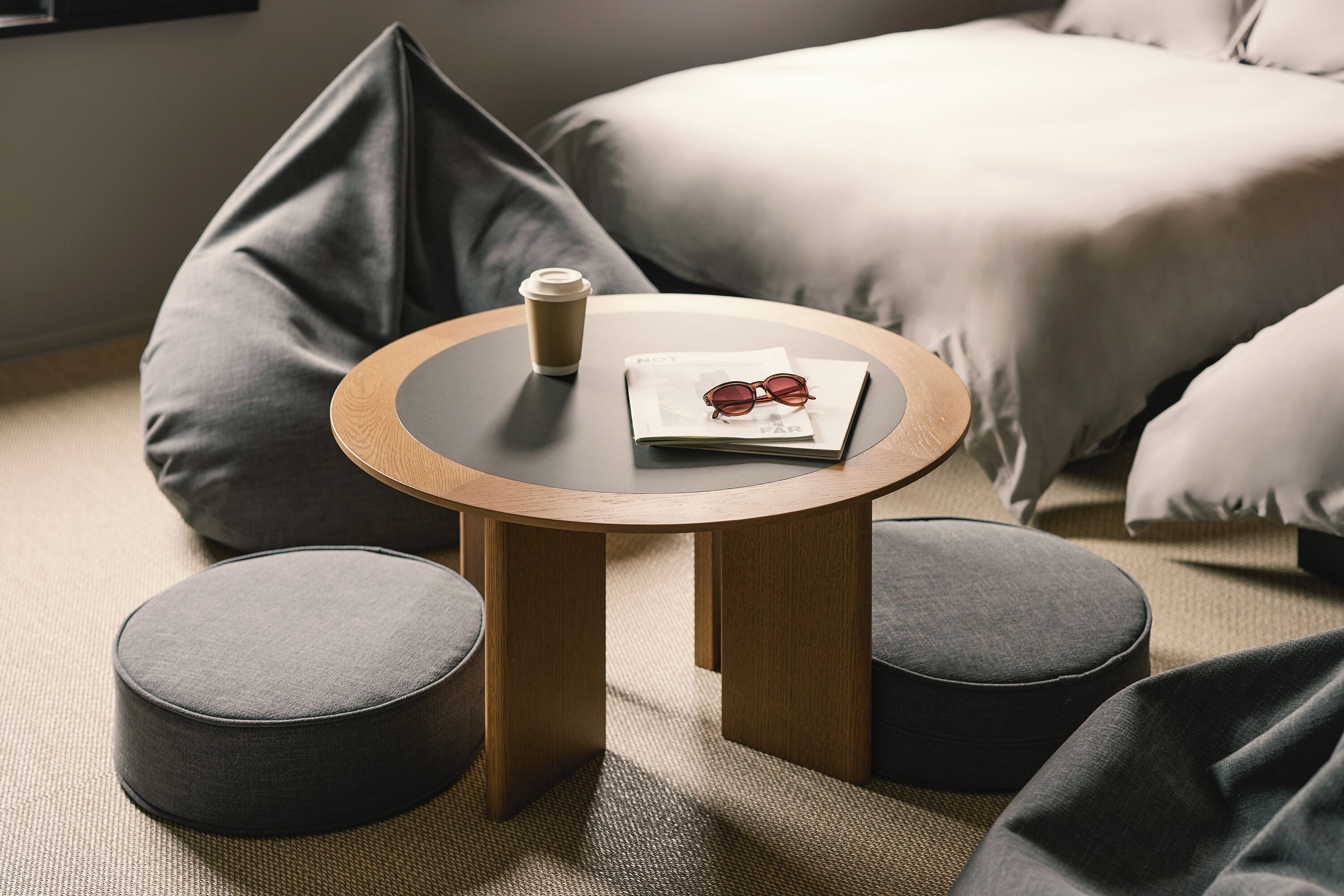 A round wooden table with a glass top, a pair of glasses, and a coffee cup on a magazine.