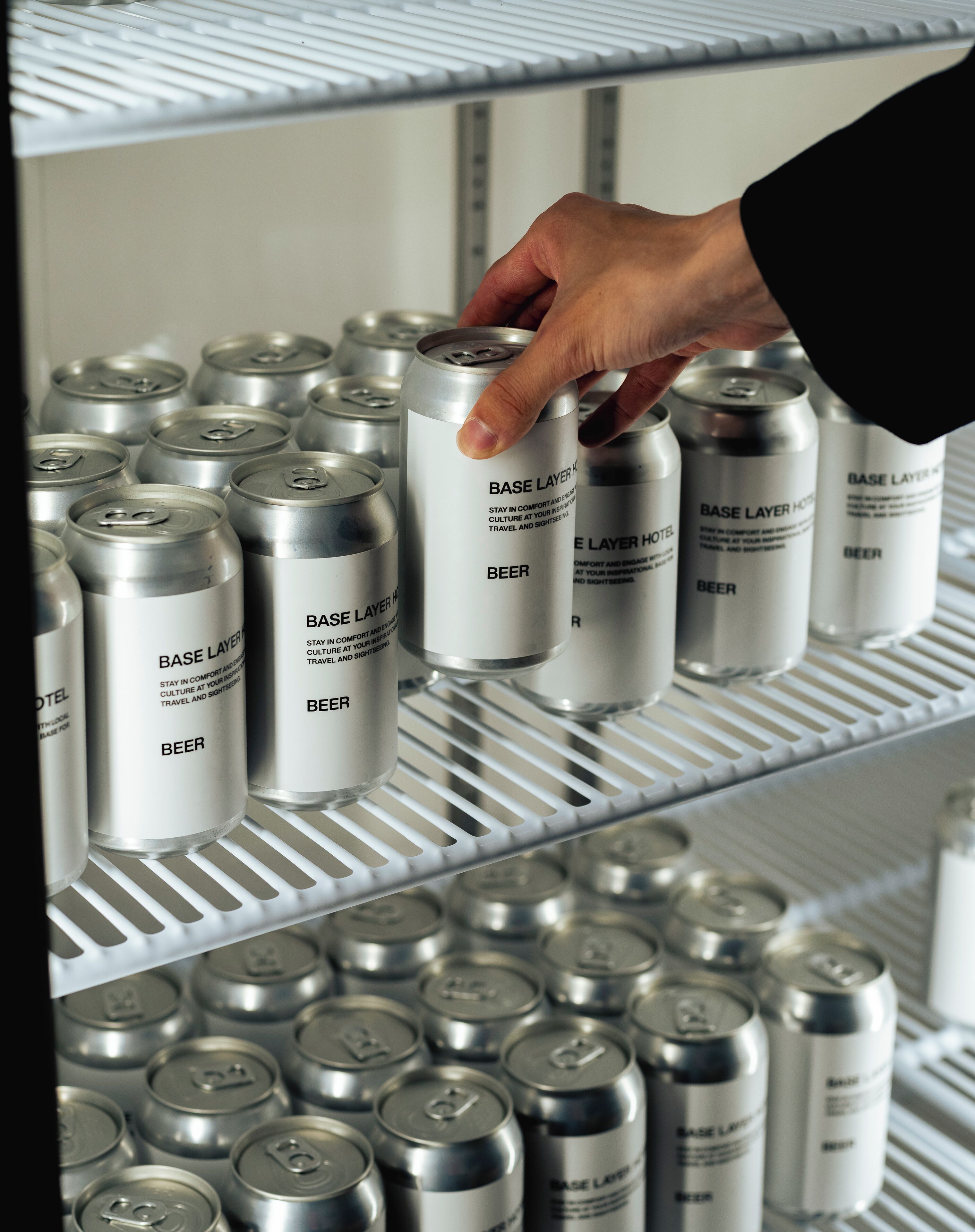 Eine Hand greift eine Dose Bier von einem Regal, das mit mehreren Dosen gefüllt ist.