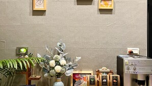 Una mesa ordenada con diferentes productos de té y una máquina de café, obras de arte decorativas en la pared y una planta ornamental.