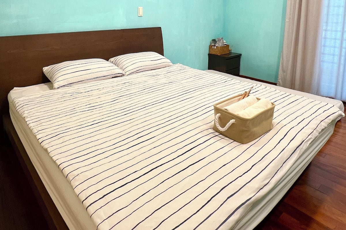 A neatly made bed with striped bedding in a room with teal walls and wooden flooring.