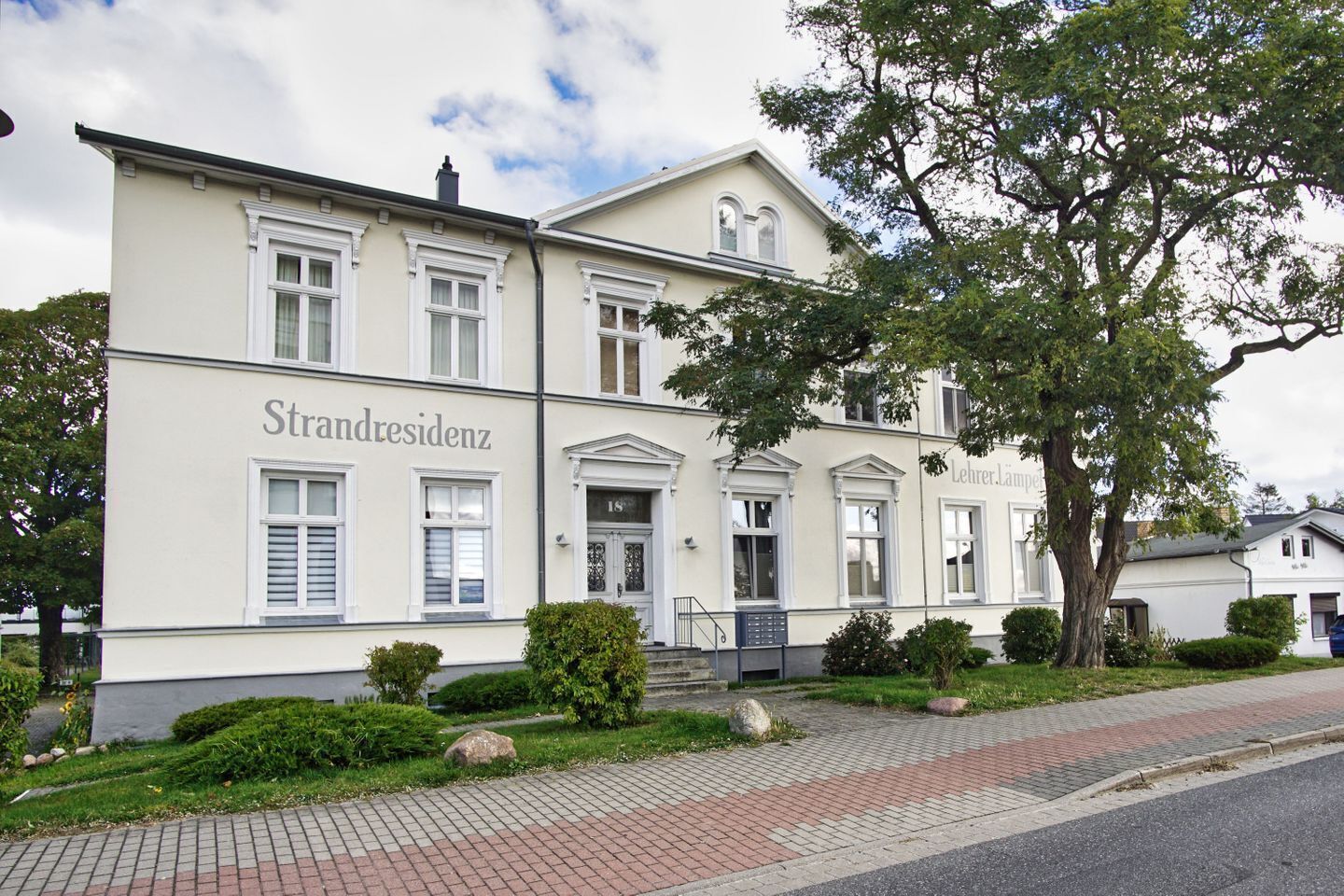 Um edifício com o nome 'Strandresidenz' na fachada, apresentando estilo arquitetônico clássico com janelas simétricas e uma entrada central.