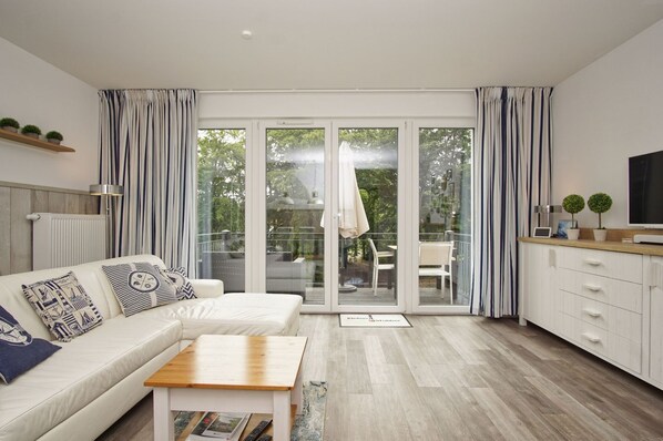Una sala de estar moderna con un sofá, una mesa de centro y vistas a un patio exterior a través de puertas de vidrio.