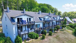 A row of three-story residential buildings with balconies, surrounded by greenery and trees. - Residence Waldidyll FeWo Kleiner Stubber - with use of the swimming pool at AHOI Sellin - (Sellin)