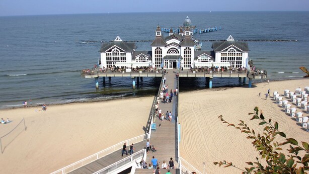 A pier leading to a large building with multiple windows and a dome, extending into the water. - Residence Waldidyll FeWo Kleiner Stubber - with use of the swimming pool at AHOI Sellin - (Sellin)