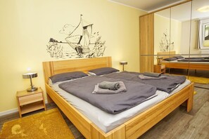 A double bed with a wooden frame, two bedside tables with lamps, a large mirror, and a wall mural of a sailing ship. - Residence Waldidyll FeWo Kleiner Stubber - with use of the swimming pool at AHOI Sellin - (Sellin)