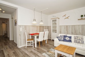 Una sala de estar moderna con un sofá blanco, una mesa de centro de madera y un comedor con mantel rojo.