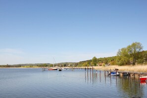 Ein ruhiger See mit Booten an hölzernen Stegen, umgeben von Bäumen und wolkenlosem Himmel.
