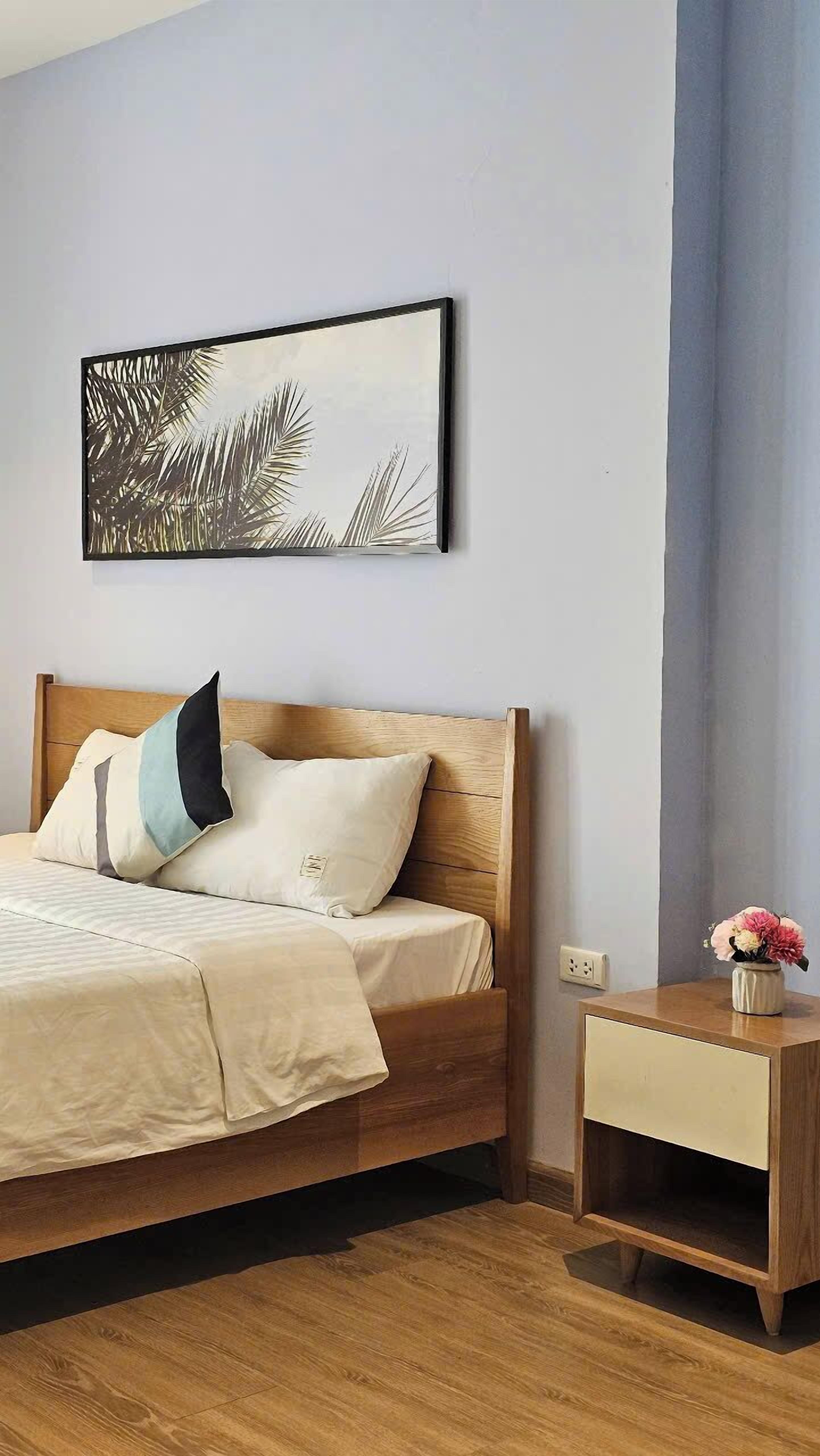 A bedroom with a wooden bed, a nightstand, a framed picture, and a vase with flowers.