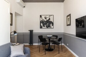 Ein modernes Wohnzimmer mit einem grauen Sofa, einem runden Esstisch mit vier Stühlen und Bildern an den Wänden.