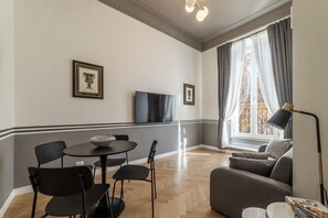 Uma sala de estar moderna com um sofá, uma mesa de jantar com cadeiras, uma televisão e uma janela com cortinas.