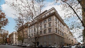 Ein mehrstöckiges Gebäude mit klassischer Architektur, mit Hauseingang an einer Ecke und einer Reihe geparkter Autos entlang der Straße.