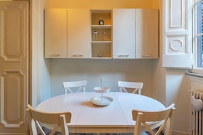 Een ronde eettafel met witte stoelen, een wit kastje erboven en een radiator aan de rechterkant.