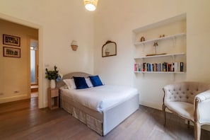 Ein Schlafzimmer mit einem Bett, Nachttischen, einem Sessel und Einbauschränken mit Büchern.