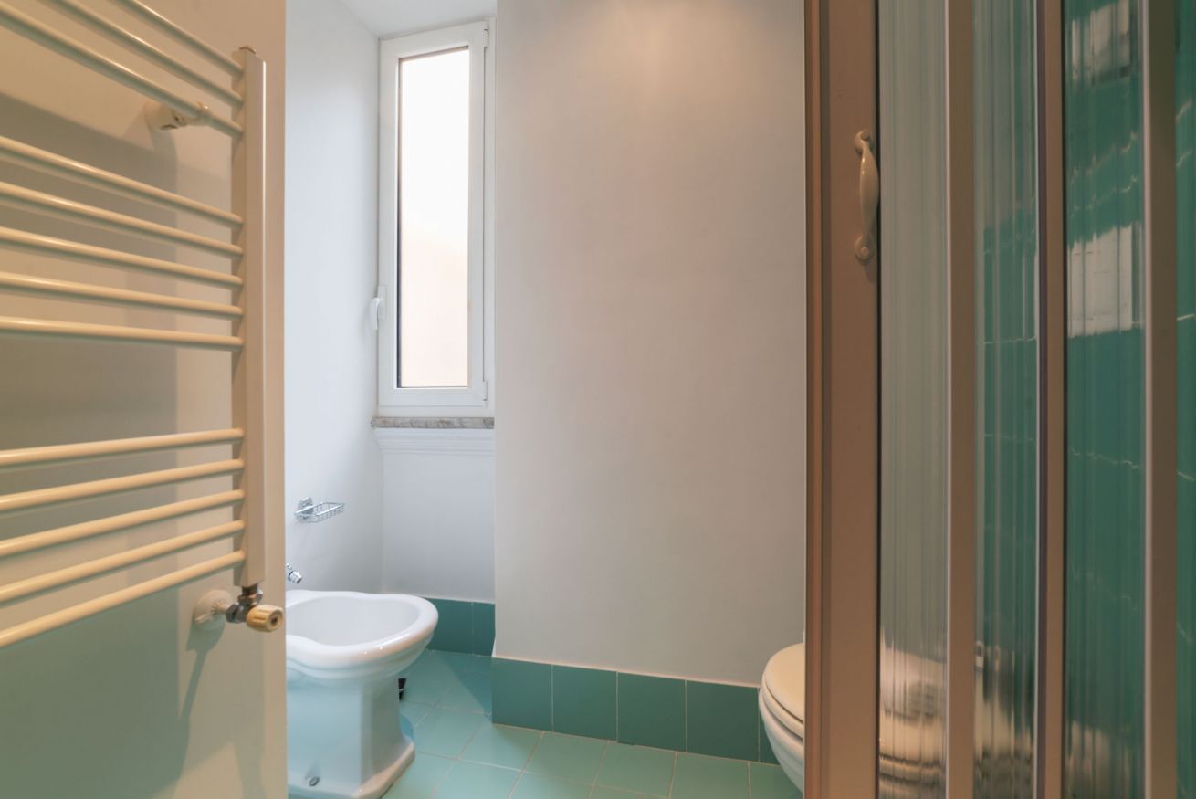 A bathroom with a toilet, a window, and a shower area.