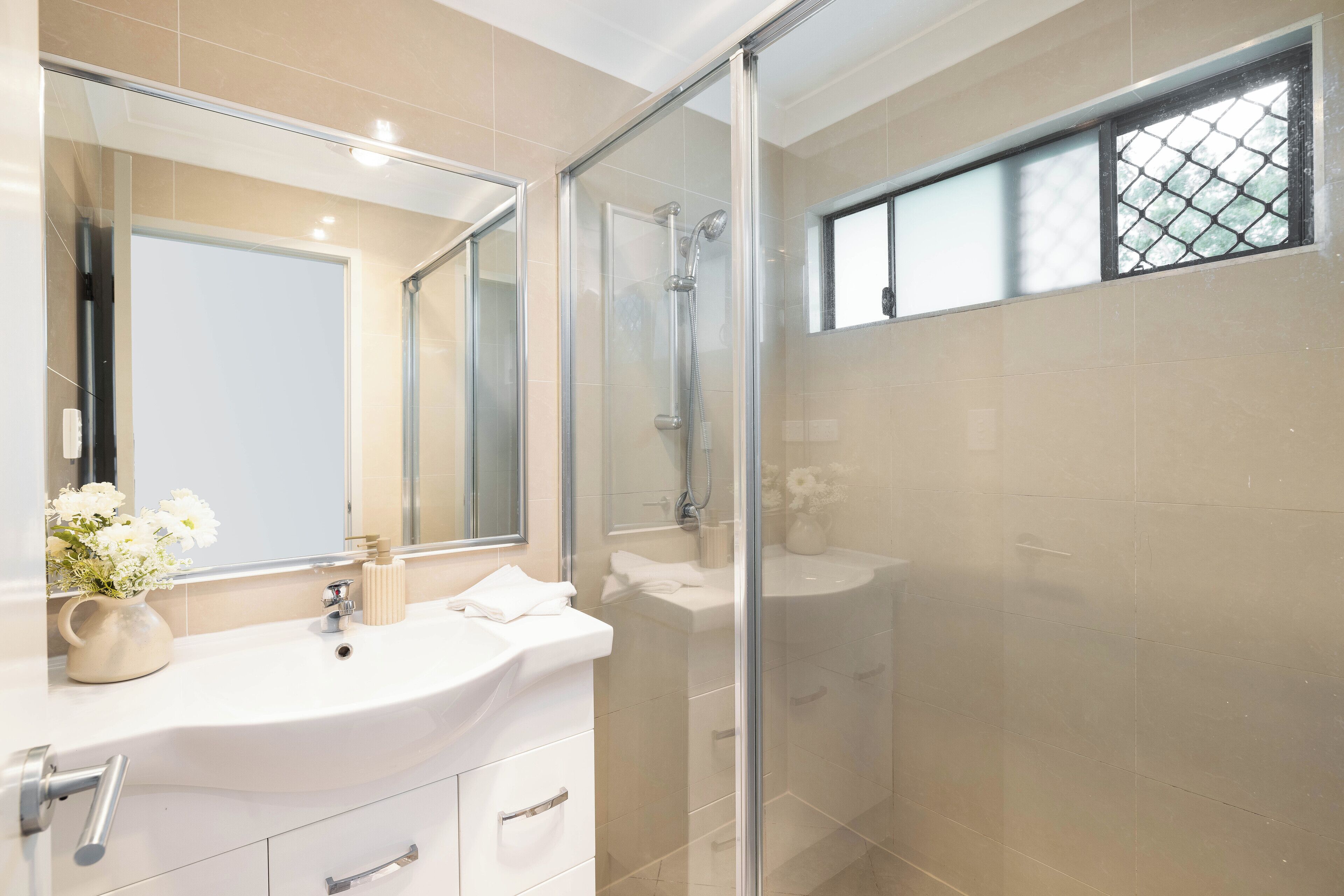 Un baño moderno con ducha envuelta en vidrio, un espejo grande y un lavamanos blanco.
