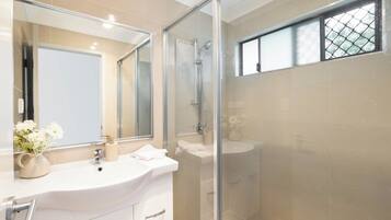 Un baño moderno con ducha envuelta en vidrio, un espejo grande y un lavamanos blanco.