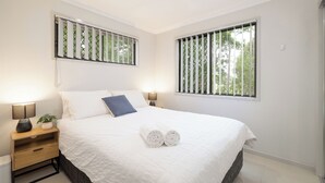 A neatly made bed with white bedding, two bedside lamps, and a small plant on the nightstand. - Smart Suites Self Check-in Apartments - 73 Bale (Rocklea)