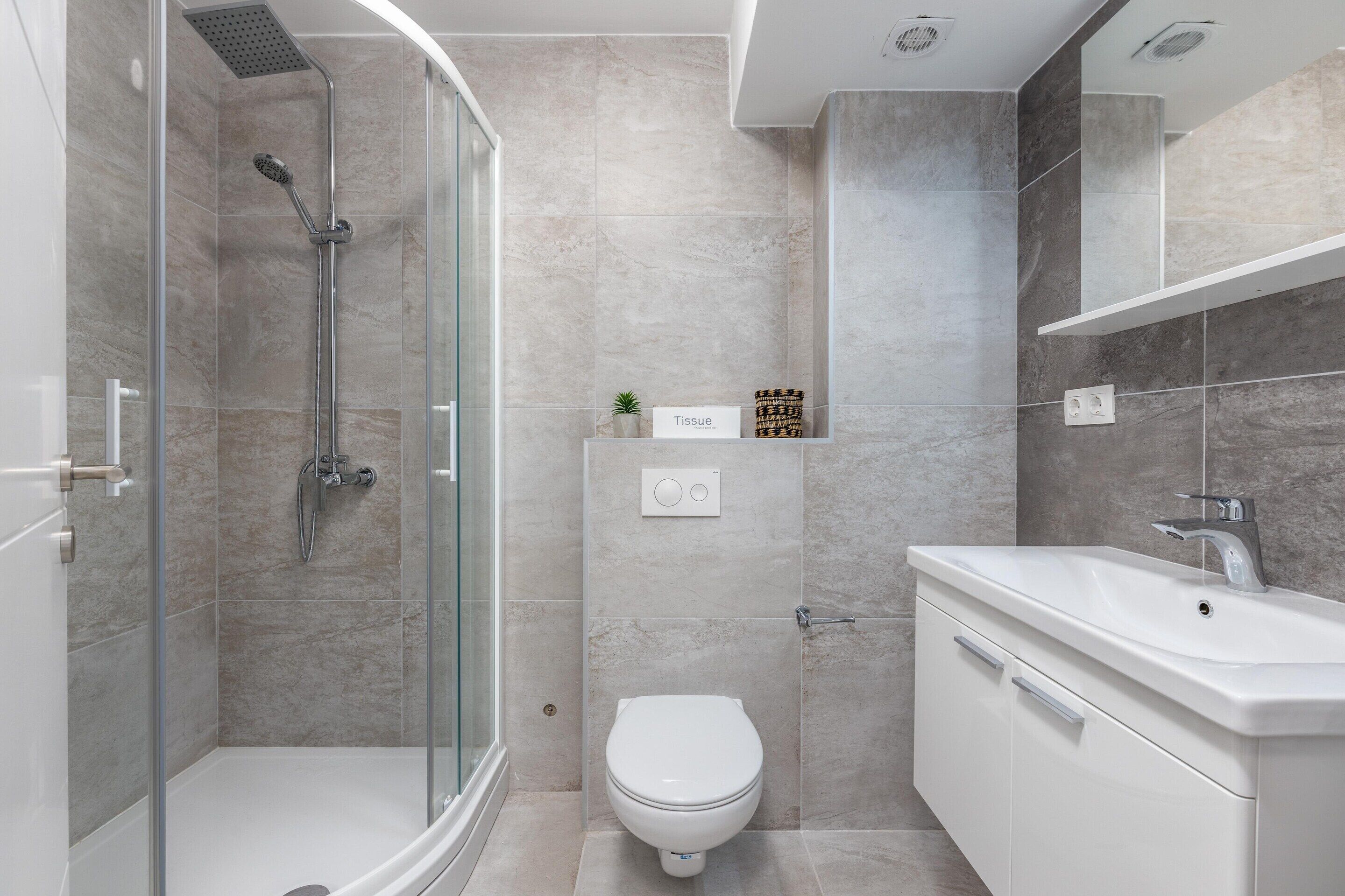 Une salle de bain moderne avec une douche à parois de verre, des toilettes blanches et un meuble-lavabo avec un évier.