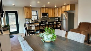 Una cocina moderna con armarios de madera, un refrigerador de acero inoxidable y un comedor con una mesa y sillas de madera oscura.