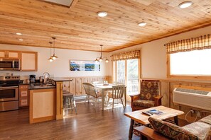 Una cocina acogedora de estilo cabaña con armarios de madera, un comedor con mesa y sillas, y una zona de estar con un sofá estampado.