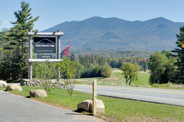 A sign for Cobble Mountain Lodge with a vacancy notice, set against a backdrop of mountains and a clear sky.