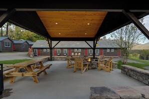 Een terras buiten met houten tafels en stoelen, een vuurkorf en een stenen muur.