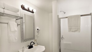Ein Badezimmer mit einem weißen Waschbecken, einem Spiegel mit Beleuchtung, einem Fön und einer Duschkabine aus Glas.