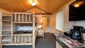 Ein rustikales Cabin-Zimmer mit einem Etagenbett, einem kleinen Tisch mit Lampe, einer Kaffeemaschine und einem an der Wand montierten Fernseher.