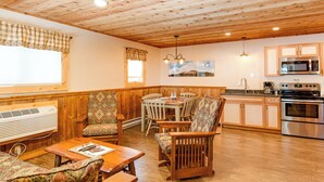 A cozy cabin interior with a wooden ceiling, a dining area with patterned chairs, a kitchen with modern appliances, and a large window providing natural light. - Cozy 3Bedroom w/2 Bath and Full Kitchen, Outdoor BBQ, Fire Pits (Lake Placid)