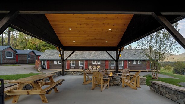 An outdoor patio with wooden tables and chairs, a fire pit, and a stone wall. - Cozy 3Bedroom w/2 Bath and Full Kitchen, Outdoor BBQ, Fire Pits (Lake Placid)