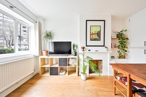 A modern living room with a TV, wooden shelves, a fireplace, and a dining area. - GuestReady - Cosy and bright home in Islington (London)