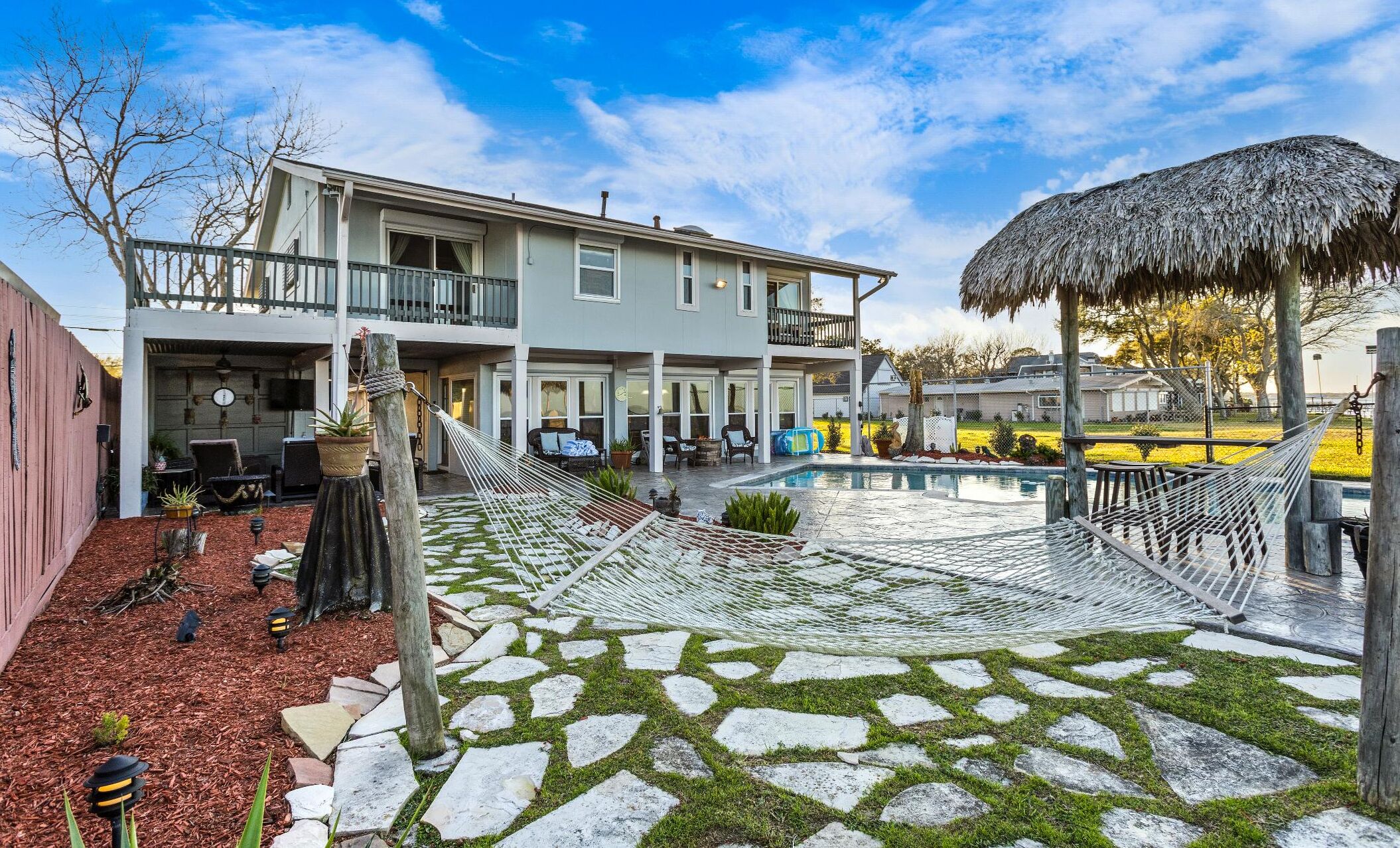 A two-story house with a pool, a hammock, and a thatched roof structure.