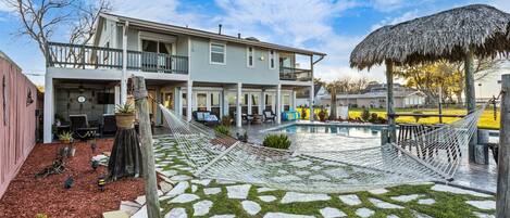 A two-story house with a pool, a hammock, and a thatched roof structure.