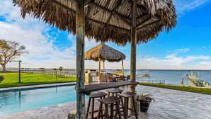 A poolside area with a wooden deck, a thatched gazebo, and a view of the ocean.