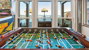 A foosball table with a view of a beach through three windows.