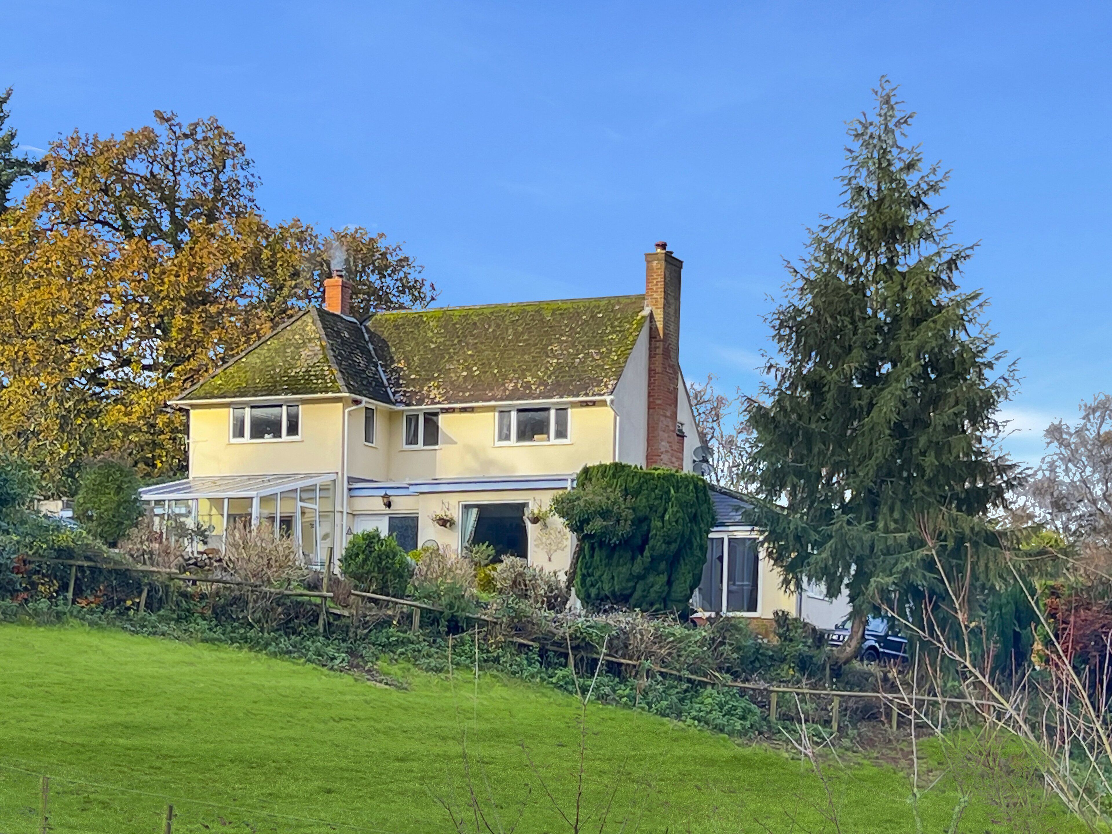A two-story house with a sloped roof, a chimney, and a conservatory.