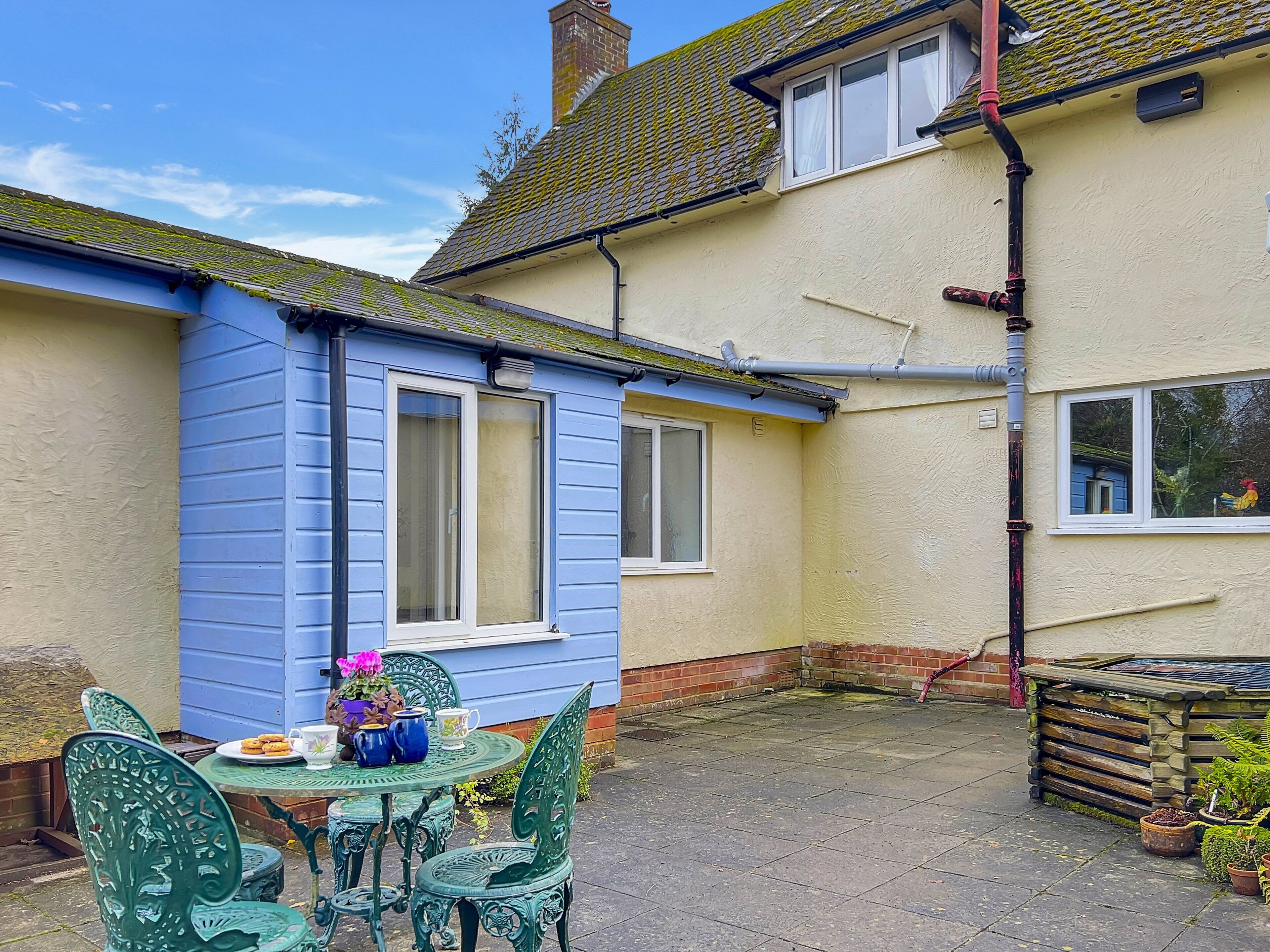 A blue house with a patio area featuring a table and chairs, a small garden, and a visible chimney.