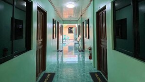 Un long couloir étroit aux murs verts et au sol en marbre, qui mène à une pièce lumineuse dotée d’un ventilateur de plafond.
