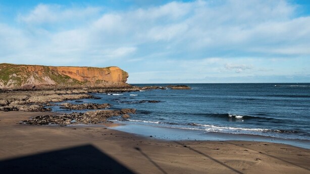 Une plage bordée d’une côte rocheuse et d’une falaise.
