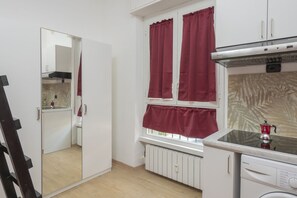 Eine kleine Küche mit weißen Schränken, einem eingebauten Herd und einem Fenster mit roten Vorhängen.