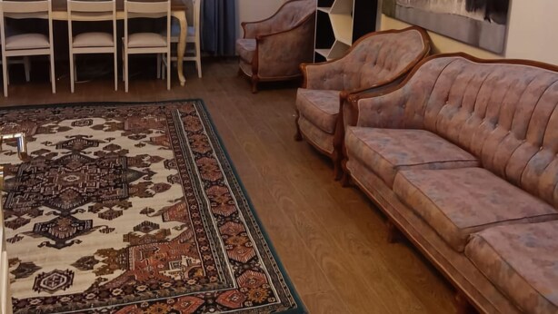 Una sala de estar con un tapete estampado, un sofá, una mesa de comedor con sillas y una lámpara moderna.
