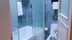 Un baño con ducha de vidrio, inodoro y un taburete de madera pequeño.