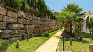 A stone retaining wall with a paved walkway, palm trees, and a clear blue sky. - Modern, ground floor Casares Playa (Casares)