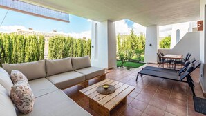 A modern outdoor living space with a sofa, a wooden table with a candle, and a dining area with chairs. - Modern, ground floor Casares Playa (Casares)