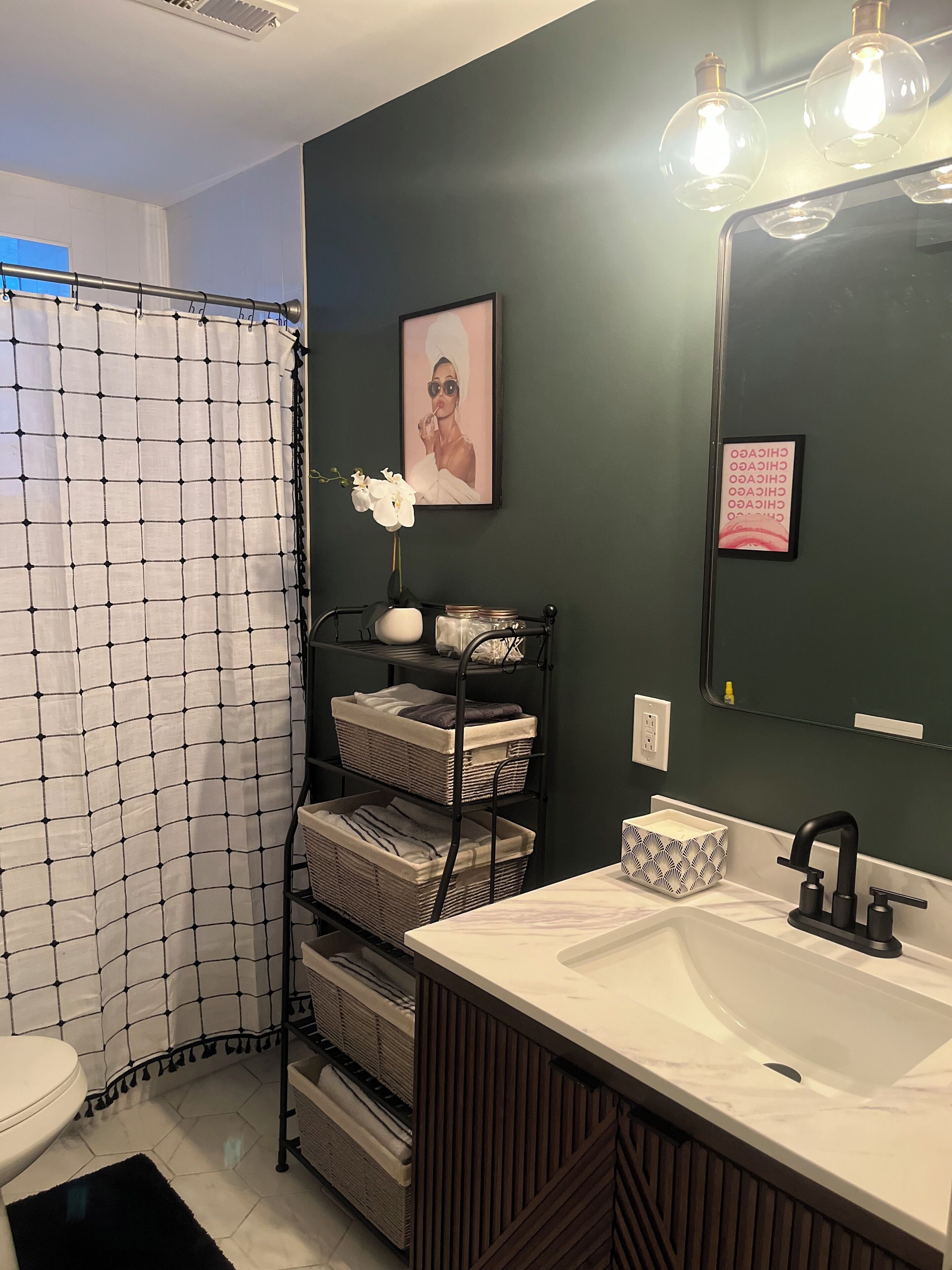 Une salle de bain avec un lavabo blanc, des murs vert foncé, un rideau de douche et une étagère avec des serviettes pliées.