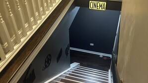 A staircase with a dark wooden finish and white balusters, leading to a cinema room.