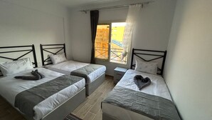A room with two single beds, each with a headboard and pillows, a small bedside table, and a window with curtains. - Bayview Apartments Sahal Hasheesh  (Hurghada)