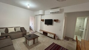 Una sala de estar con sofá, mesa de centro, televisor y un banco.
