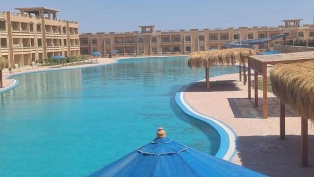 A swimming pool with a blue umbrella, surrounded by buildings with a consistent architectural style. - Bayview Apartments Sahal Hasheesh  (Hurghada)